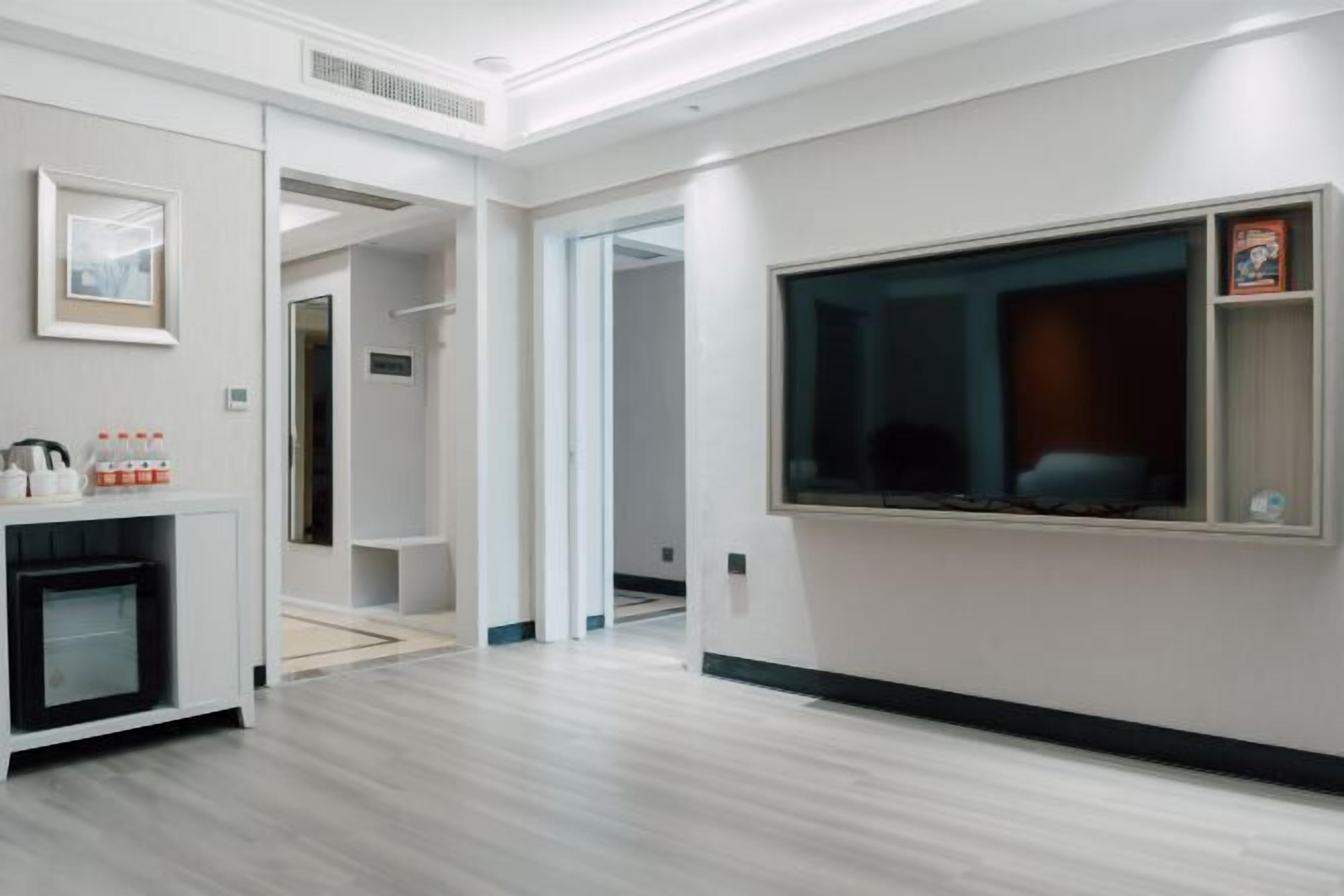 A modern hotel room with a large window, a built-in TV, and a minibar.