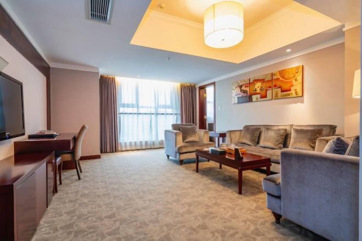 A hotel room with a sofa, armchairs, a coffee table, a desk, and a television.