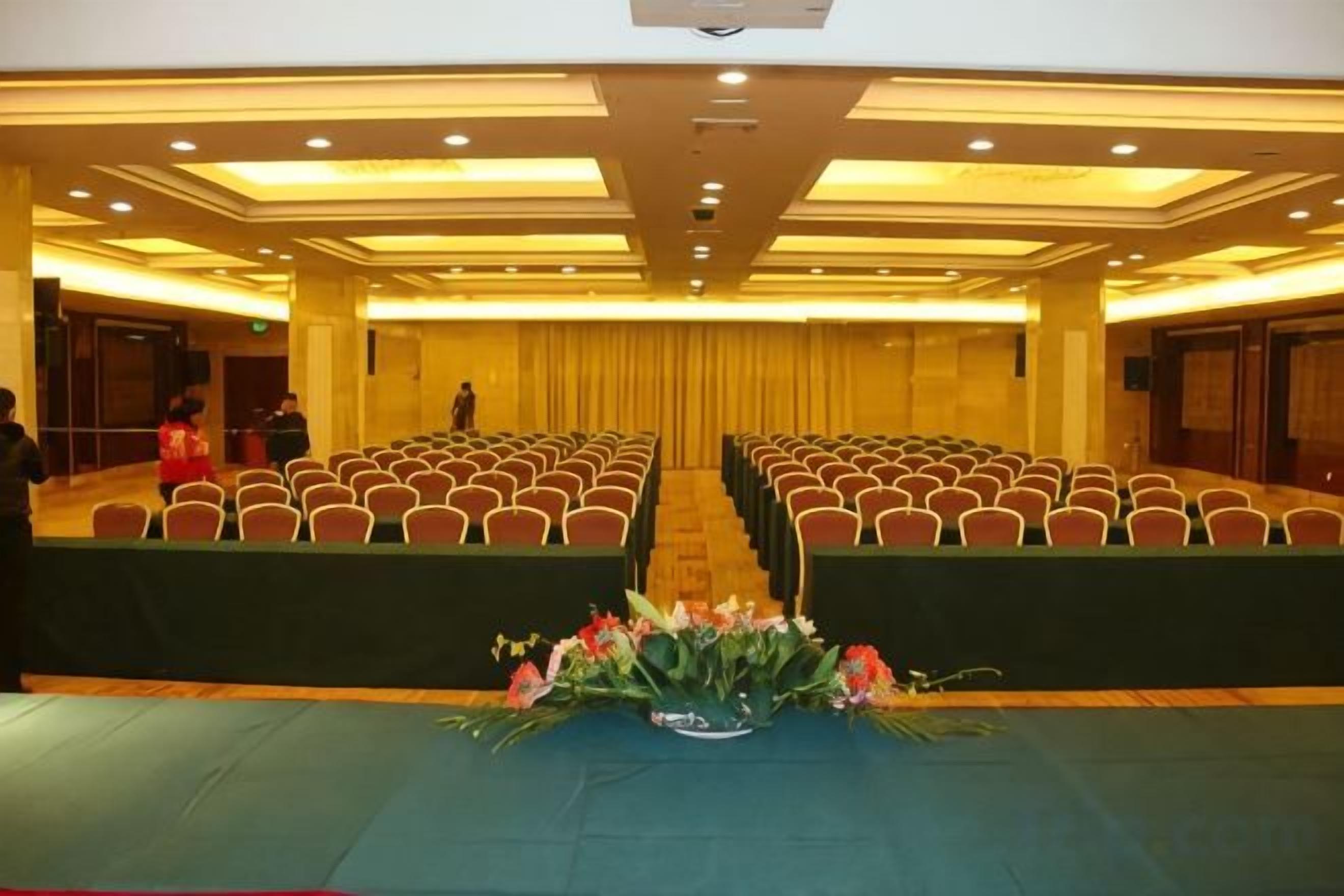 Un salón de conferencias con filas de sillas, un escenario y una mesa con flores.