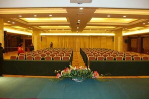 Un salón de conferencias con filas de sillas, un escenario y una mesa con flores.