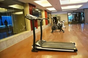 A gym with treadmills and stationary bikes, a glass wall, and a wooden floor. - Jianning Hotel (Jianning)