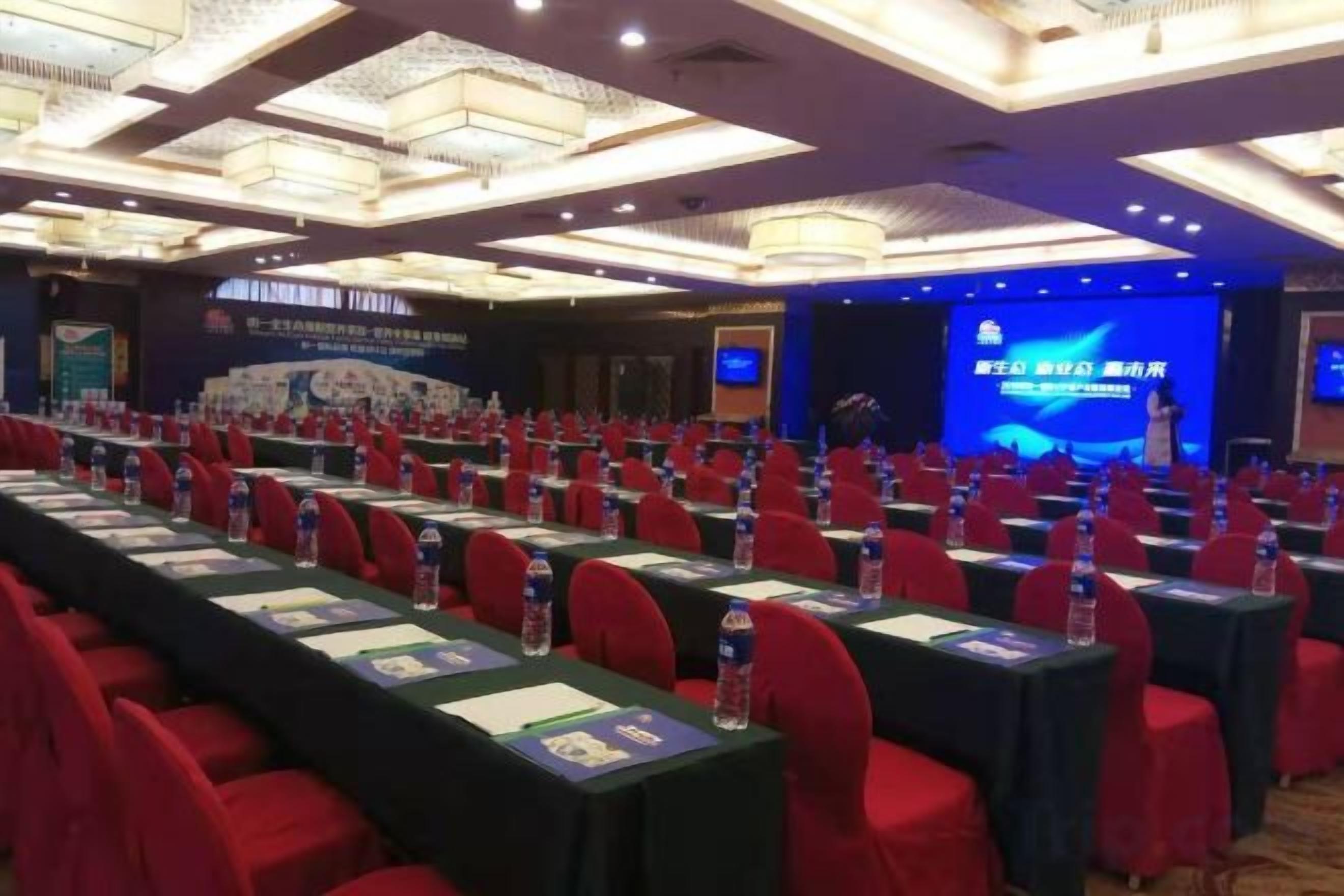 A conference room with rows of tables, chairs, and a stage with a presentation screen.