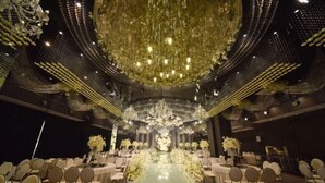 A formal event space with a central stage, rows of round tables, and ornate chandeliers.