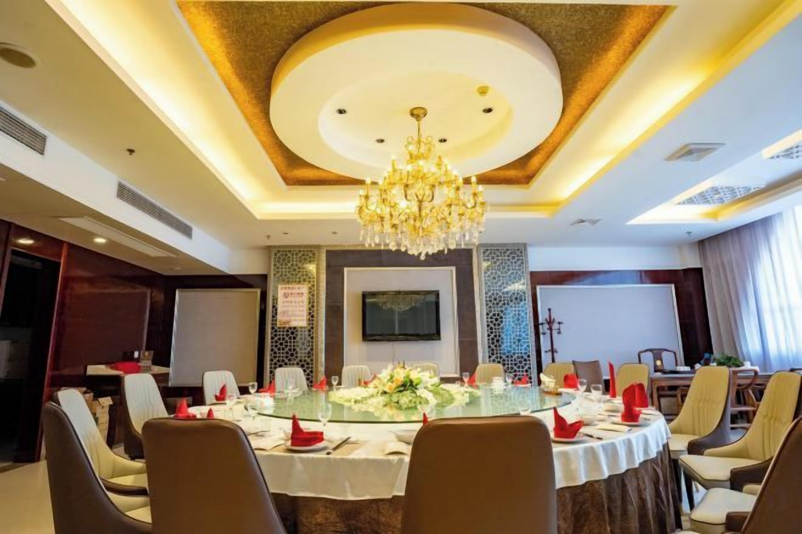 A conference room with a round table, chairs, a chandelier, and a television screen.