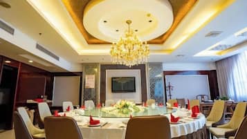 A conference room with a round table, chairs, a chandelier, and a television screen.