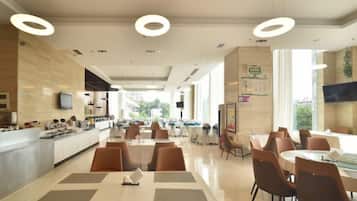 A spacious dining area with multiple tables and chairs, a kitchen area with a counter, and large windows providing natural light.