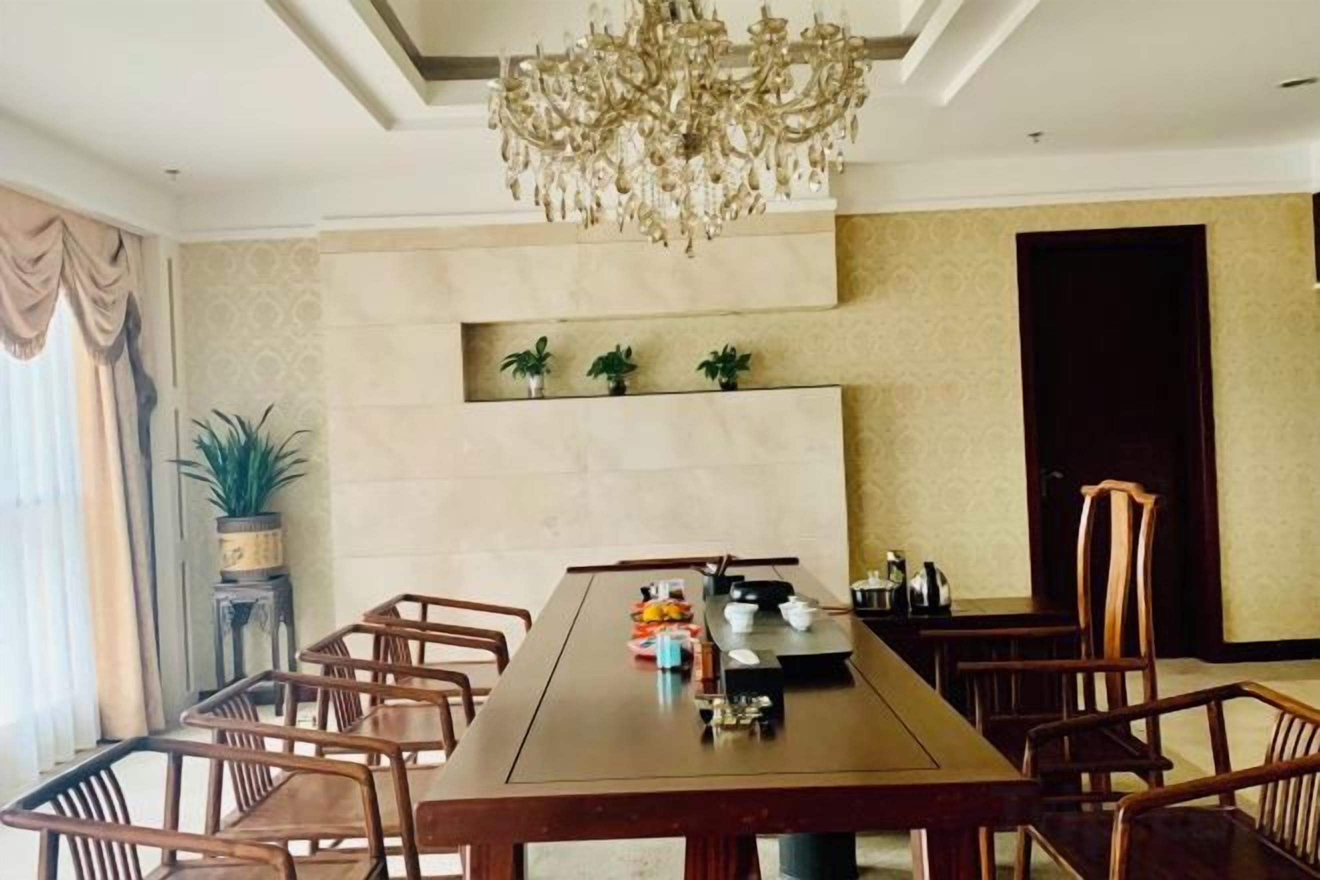 Un comedor con una larga mesa, sillas, una araña y plantas en macetas.