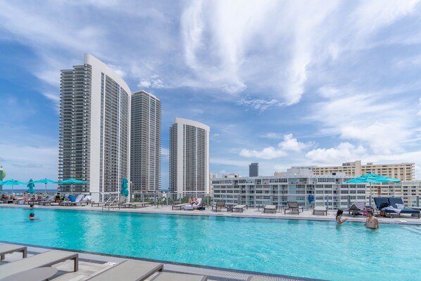 Relax by the pool surrounded by lounge chairs and umbrellas, with a view of the city skyline.