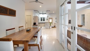 A modern dining area with a wooden table and chairs, a ceiling fan, and a view through glass doors to an outdoor space. - OriVista Charming Villa Shree Canggu 2 mins to beach (Canggu)