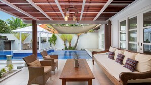 A covered outdoor seating area with a pool, wicker furniture, and a wooden table. - OriVista Charming Villa Shree Canggu 2 mins to beach (Canggu)