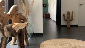 Un intérieur moderne agrémenté d’une sculpture en bois, d’un vase en verre contenant des plumes d’herbe des pampas, d’un cactus en fibres tressées et d’un tapis rond tissé.