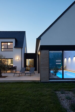 A modern house with a swimming pool, outdoor seating, and a well-lit patio area. - NEW VILLA OF 250 M², SEA VIEW, HEATED SWIMMING POOL (29°). BEACH 300M.  (Ploudalmézeau,Portsall)