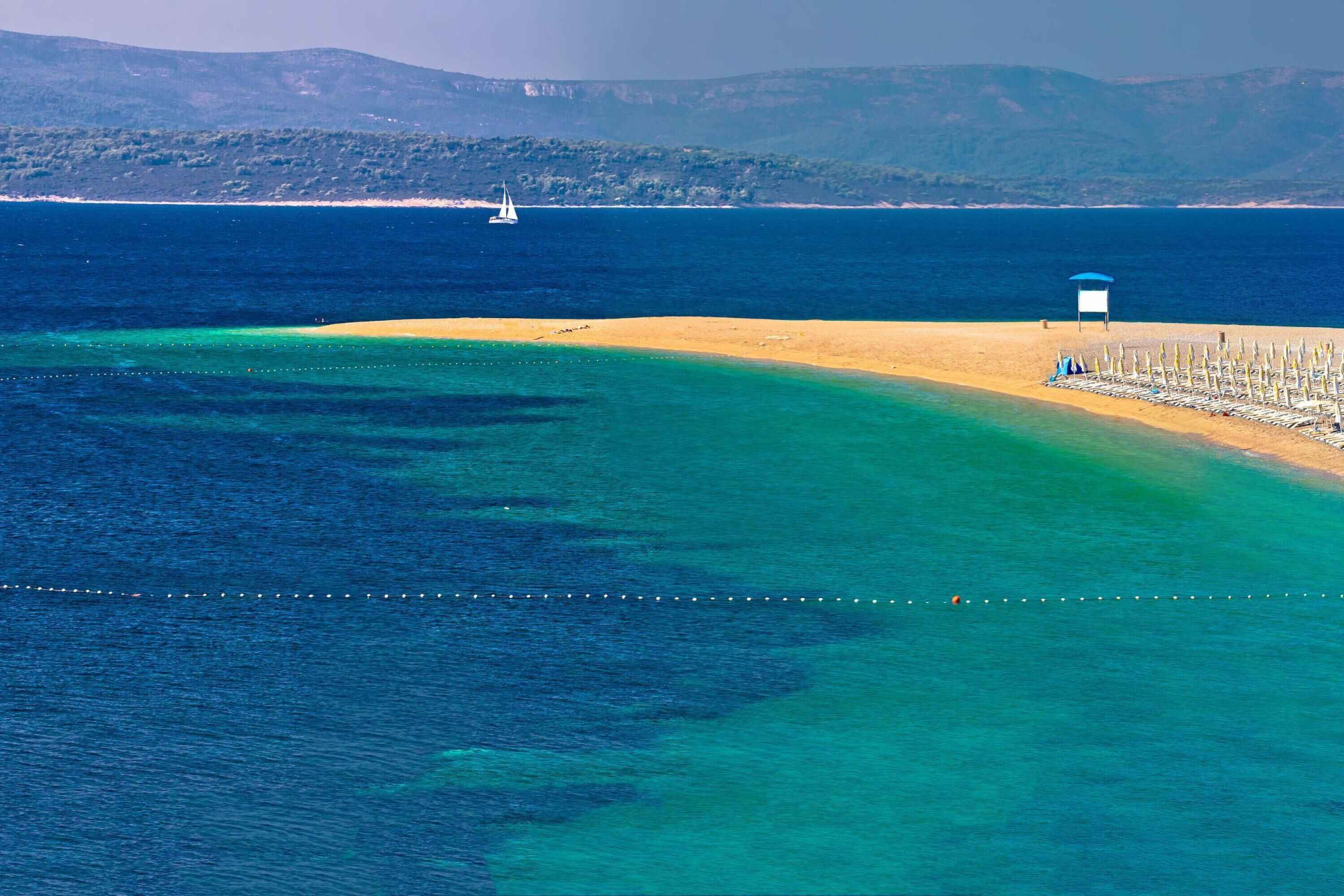 Egy tiszta vizű strand, egy vitorlás hajó és egy strandernyő.