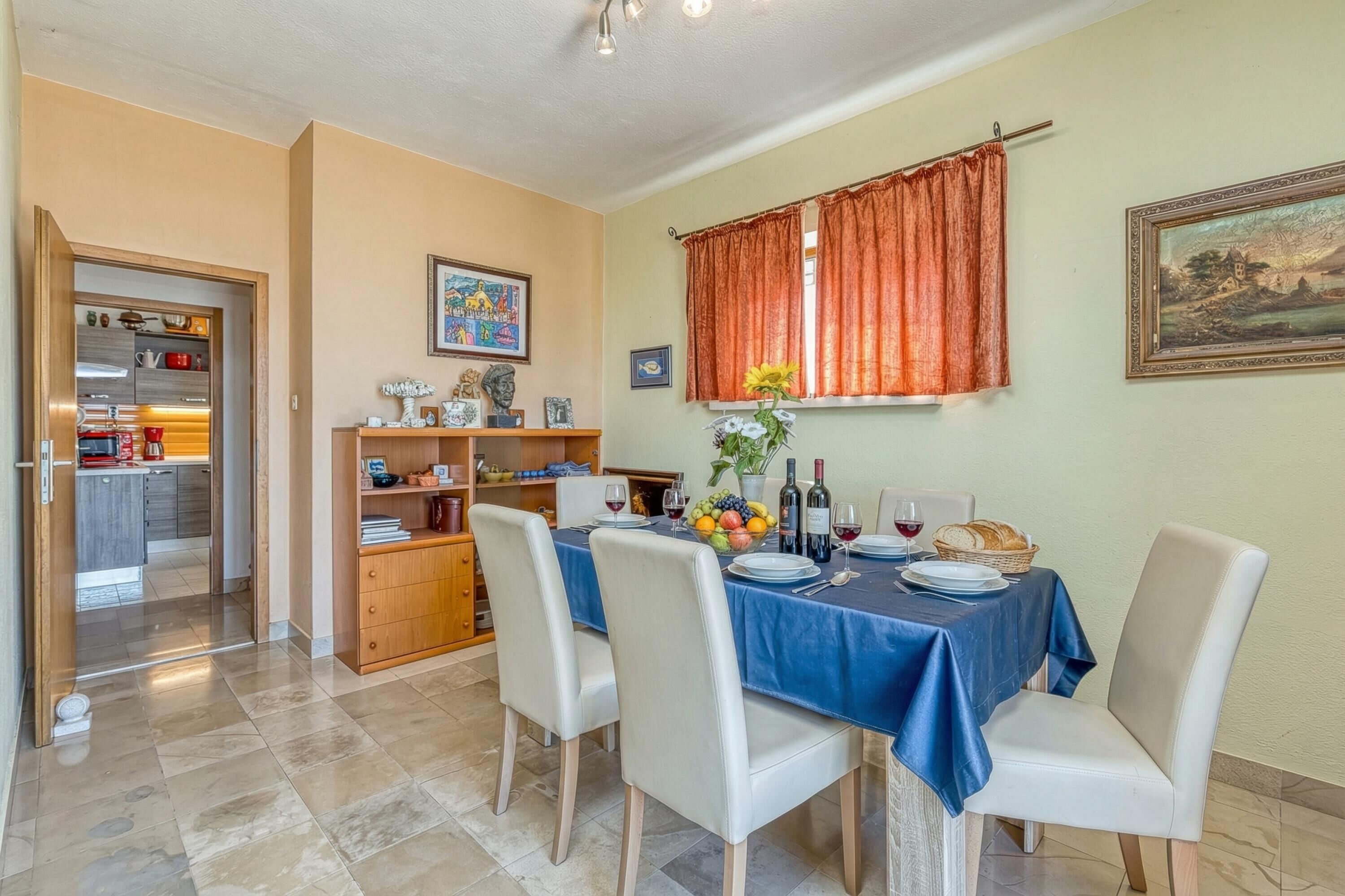 Un coin repas avec une table dressée pour quatre personnes, une cuisine en arrière-plan et une fenêtre avec des rideaux.