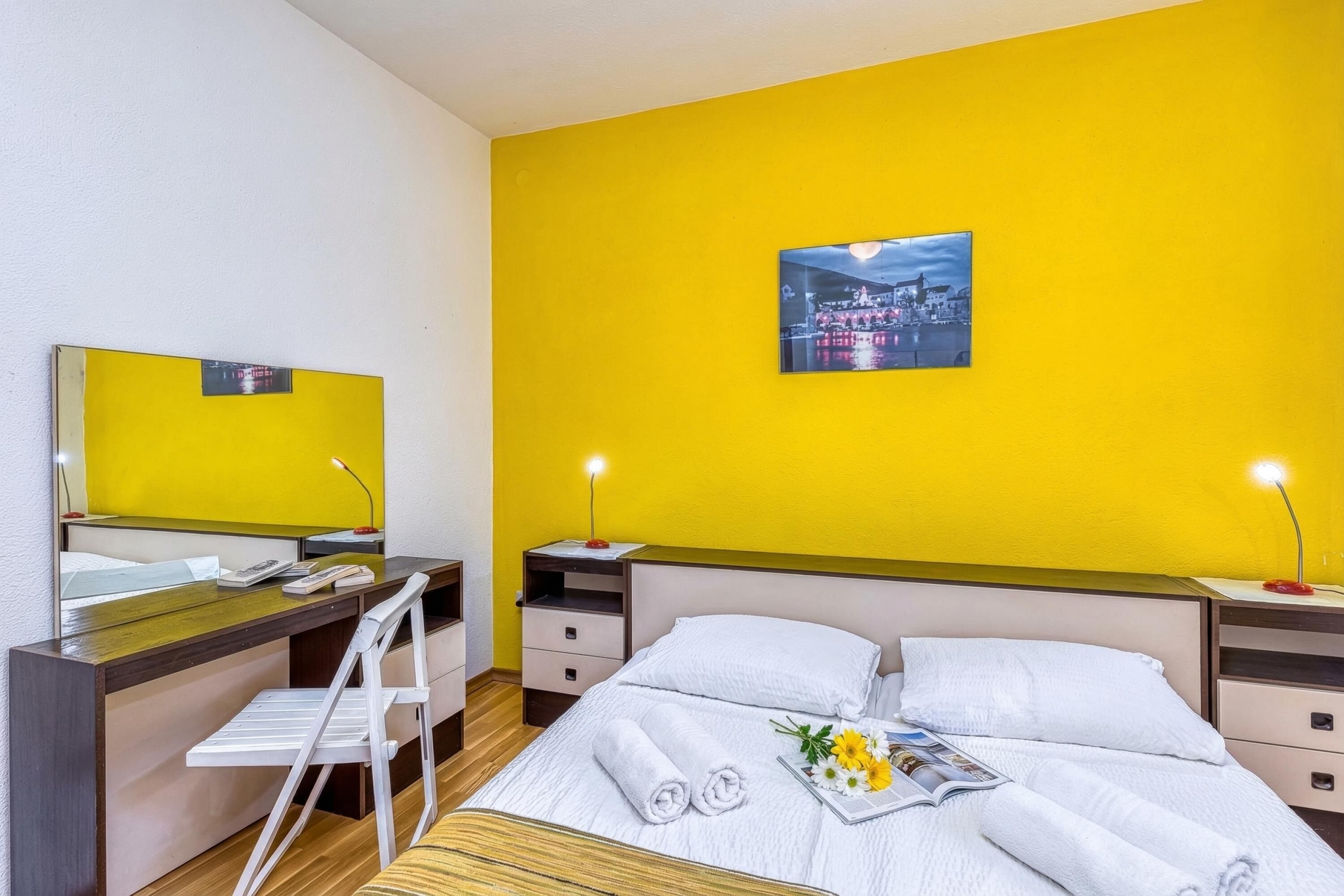 A hotel room with a bed, a desk, a chair, a nightstand, and a wall-mounted TV.