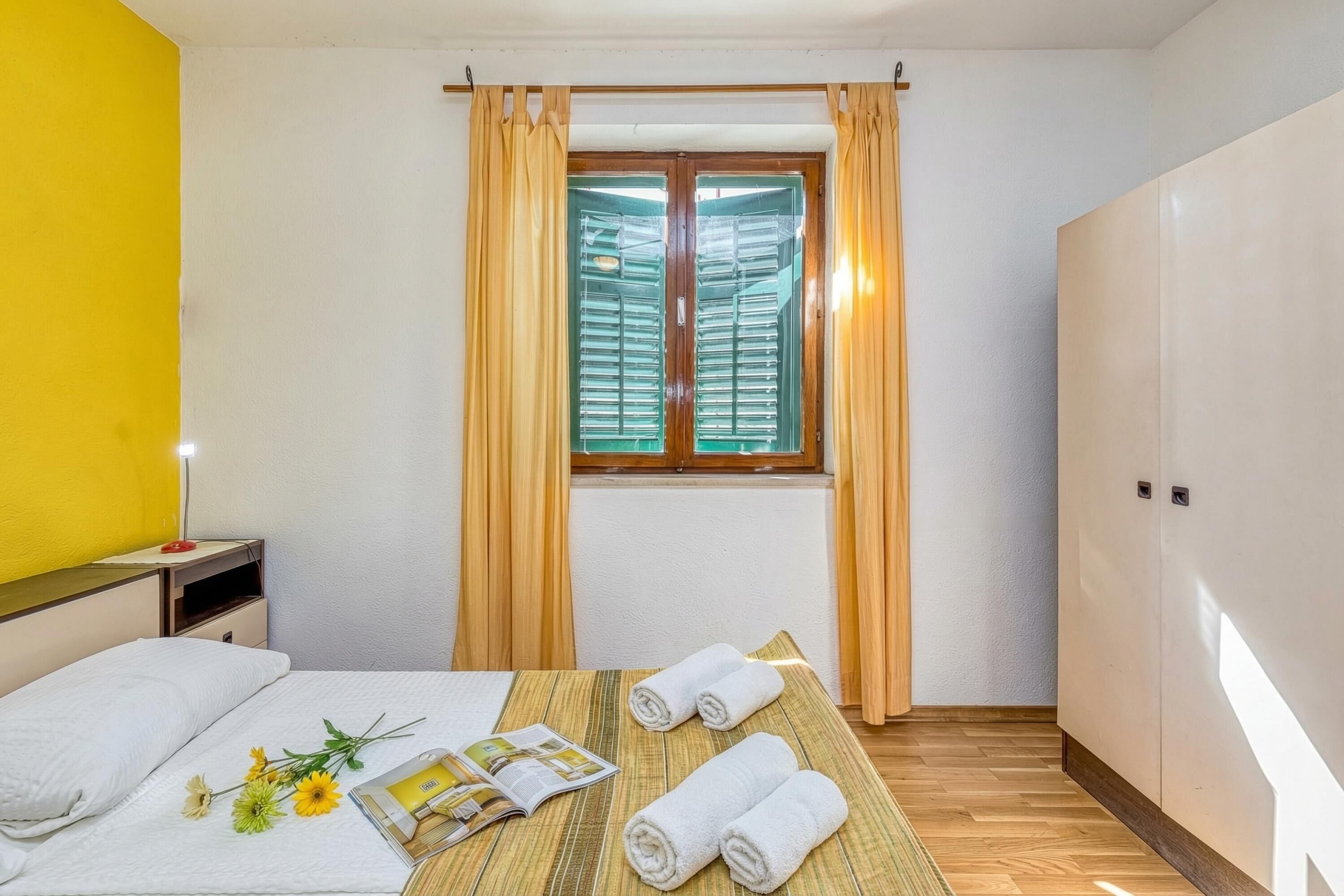 Habitació d'hotel amb un llit, una taula de nit amb una làmpada, una finestra amb cortines i un armari.