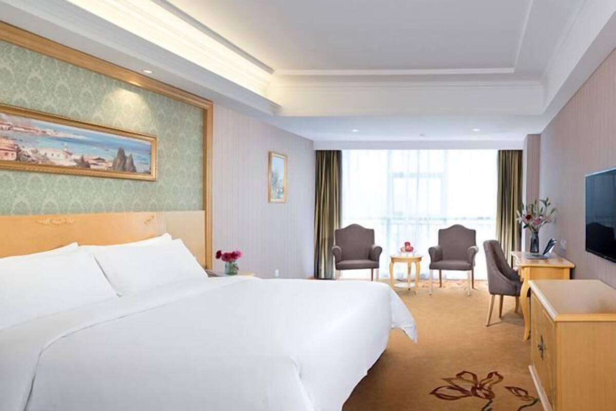 Une chambre d’hôtel avec un grand lit, un bureau, deux fauteuils, une télévision et un tableau au mur.