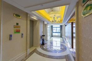Corredor de hotel com um candelabro, um balcão de recepção e vista para o saguão.