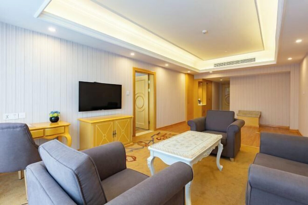 A modern living room with a flat-screen TV, grey sofas, a white coffee table, and a yellow cabinet.