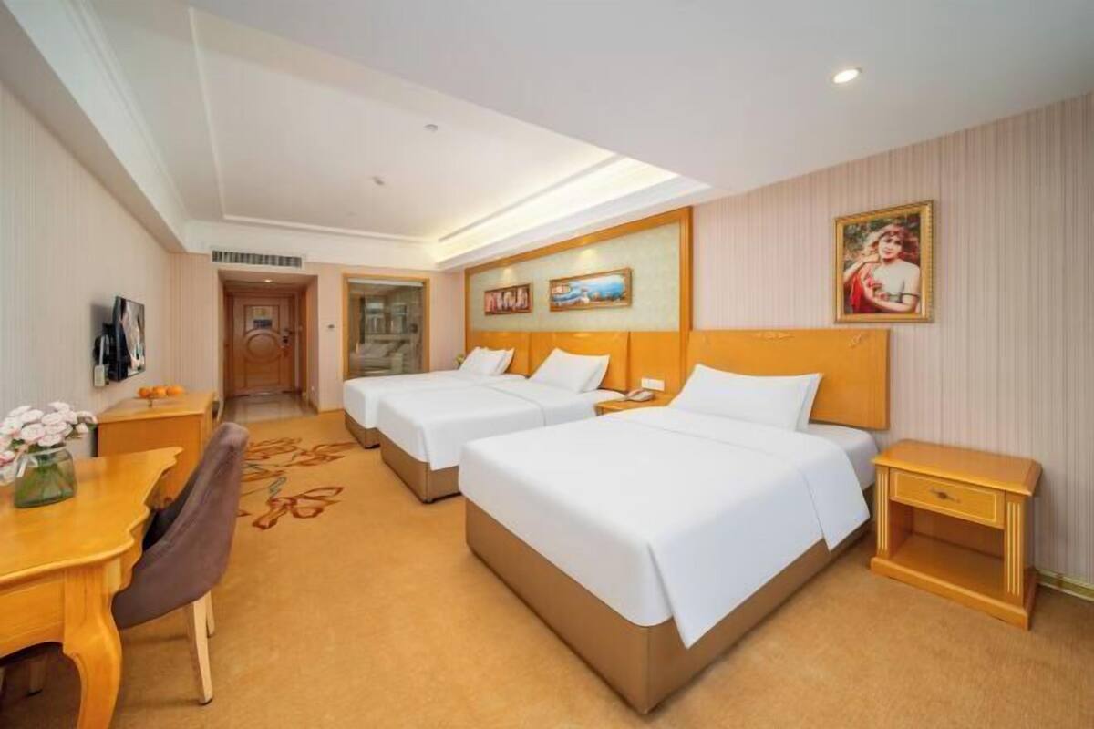Une chambre d’hôtel avec deux lits, un bureau, une chaise, une petite table et un tableau au mur.