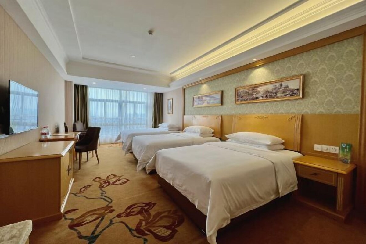 A hotel room with two beds, a desk, a chair, and a television.