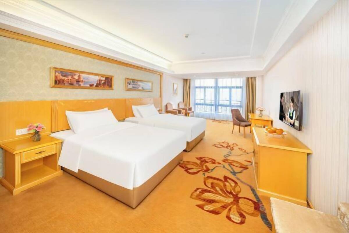 Une chambre d’hôtel avec deux lits, un bureau, une chaise, une télévision et une grande fenêtre.