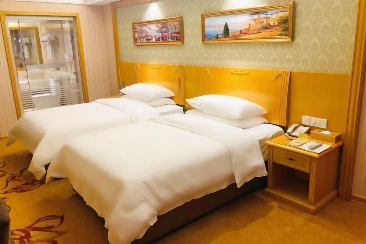 A hotel room with two beds, a bedside table with a phone, and artwork on the wall.