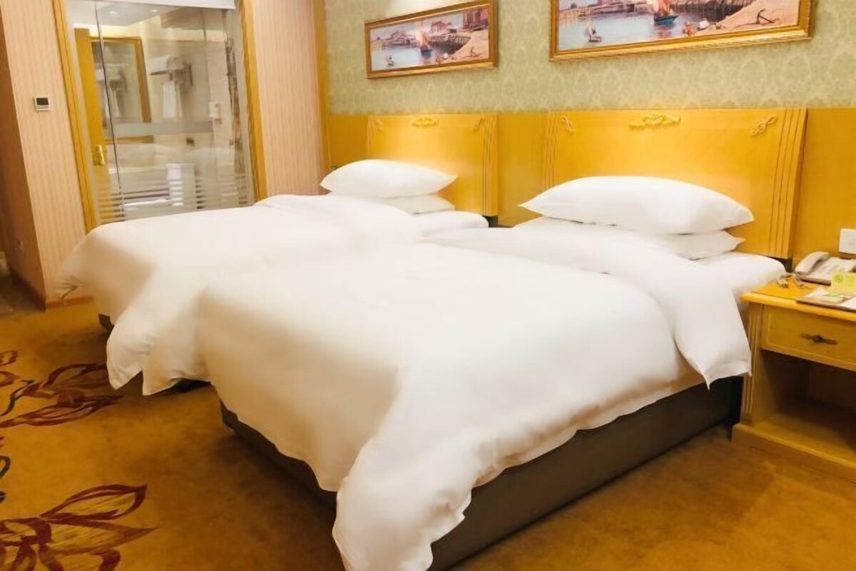A hotel room with a double bed, a bedside table with a lamp, and a mirror.