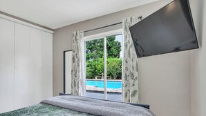 Ein Schlafzimmer mit einem Bett, einem an der Wand montierten Fernseher und einem Fenster mit Vorhängen.