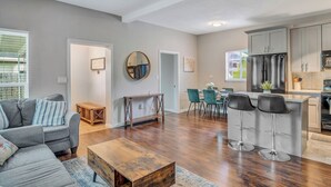 Ein geräumiges Wohnzimmer mit grauem Sofa, Holztisch und Essbereich mit blaugrünen Stühlen.