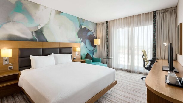 Une chambre d’hôtel moderne, dotée d’un grand lit, d’un bureau, d’une chaise et d’un grand tableau abstrait accroché au mur.