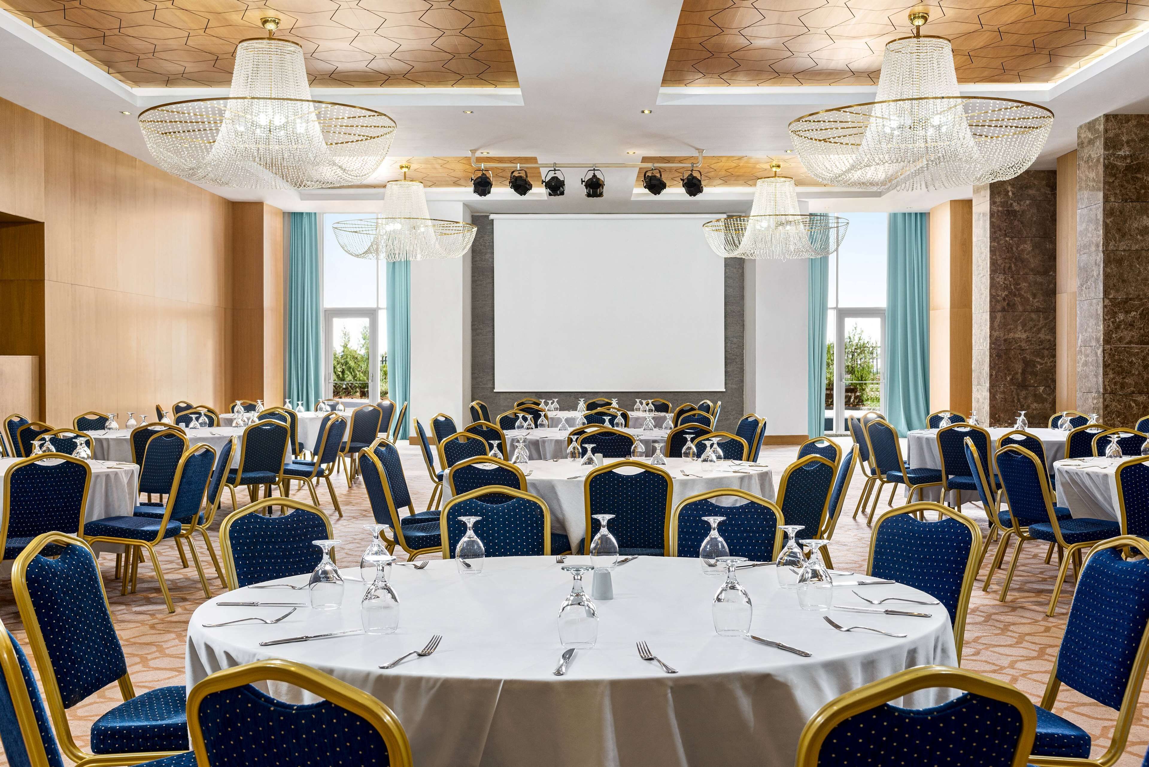 A conference room with round tables, blue chairs, and chandeliers.