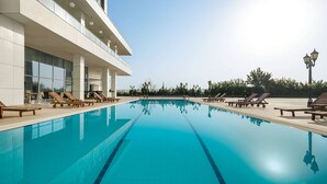 Une piscine avec des chaises longues et un bâtiment doté de grandes fenêtres.
