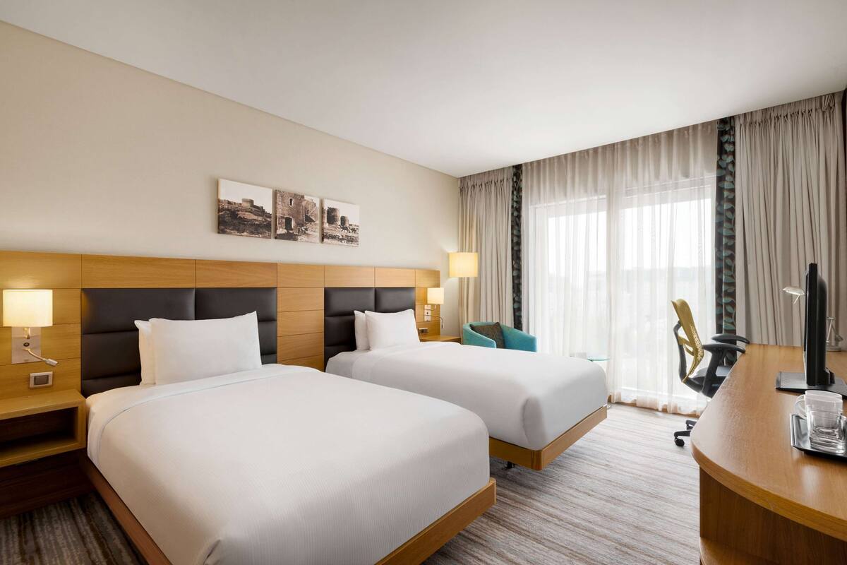 Une chambre d’hôtel avec deux lits, un bureau, une chaise, une télévision et une fenêtre avec des rideaux.