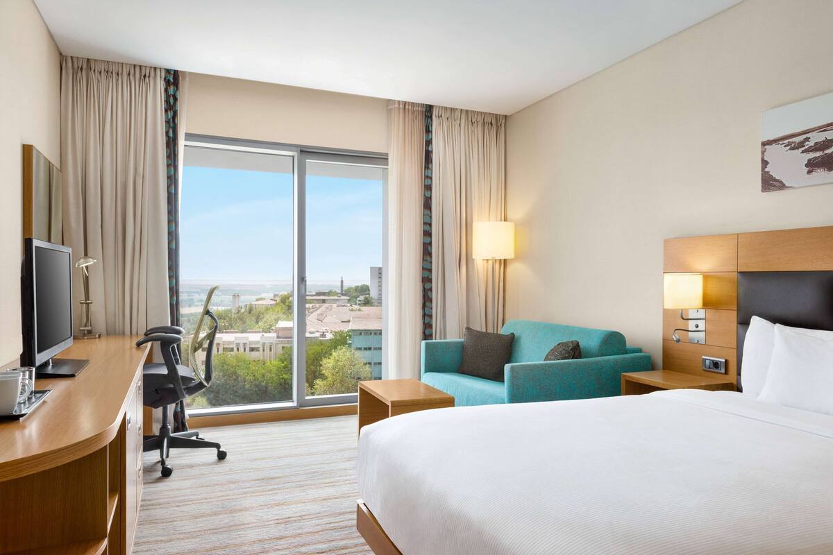 Une chambre d’hôtel avec un grand lit, un bureau avec un ordinateur, une chaise, un canapé et une vue sur la ville par la fenêtre.