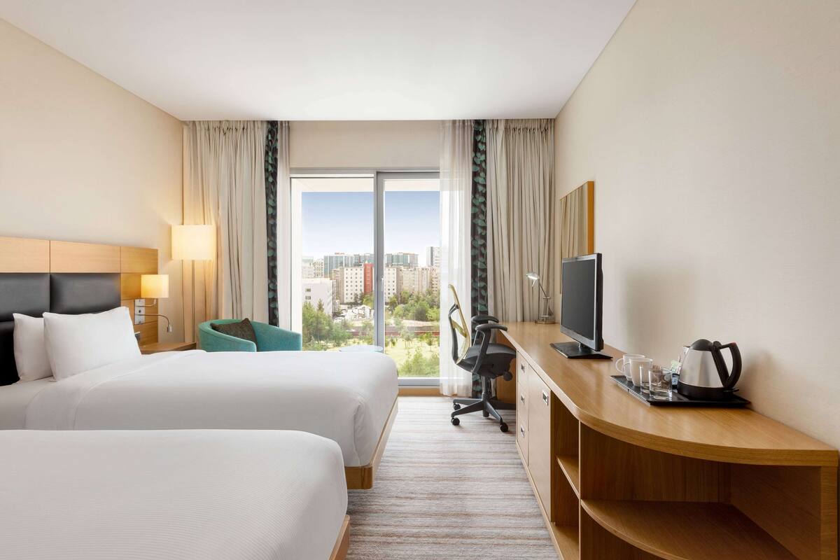 Une chambre d’hôtel avec deux lits, un bureau avec une télévision, une chaise et une vue sur la ville.