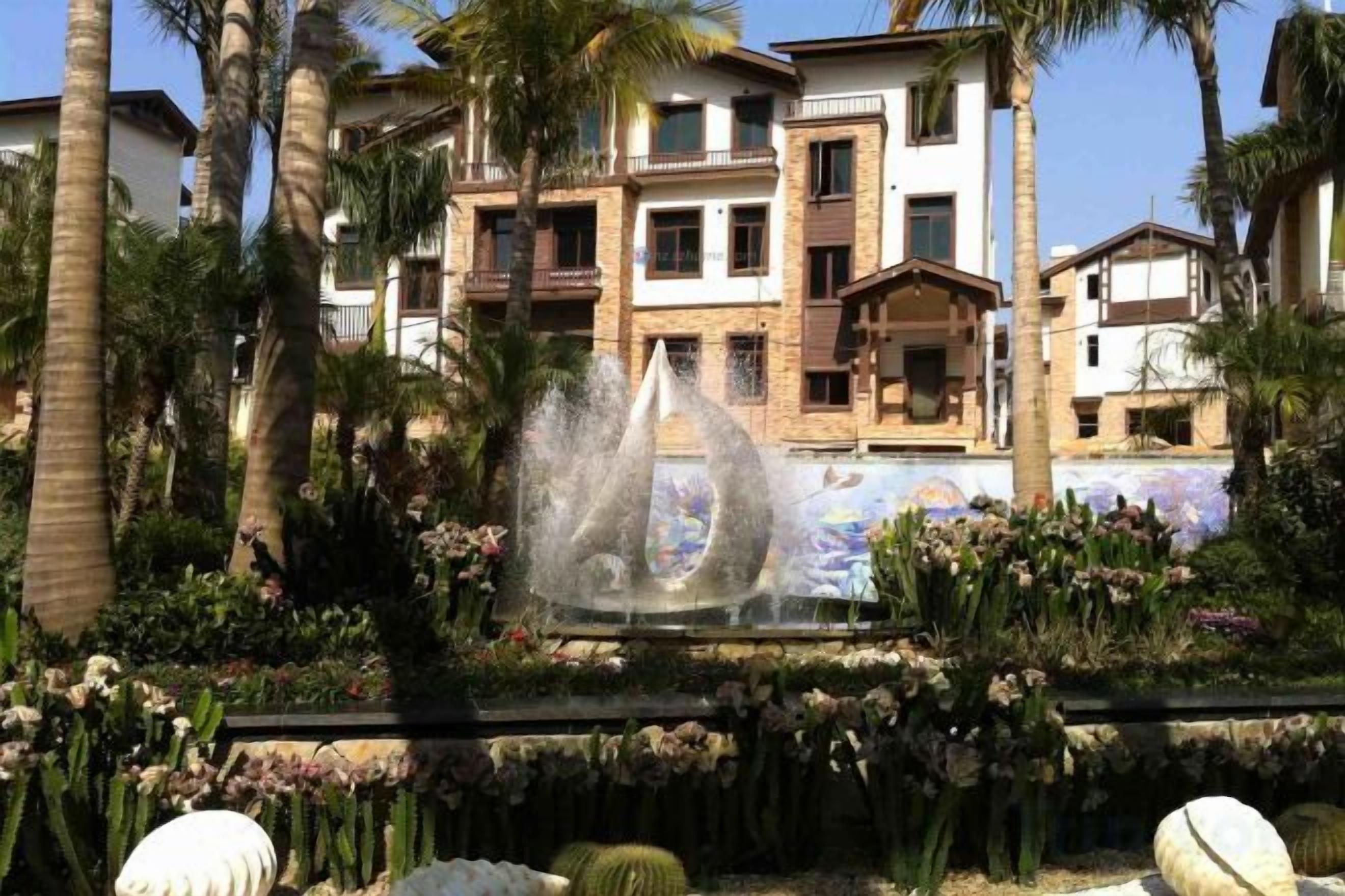 A residential building with a garden, palm trees, and a fountain.