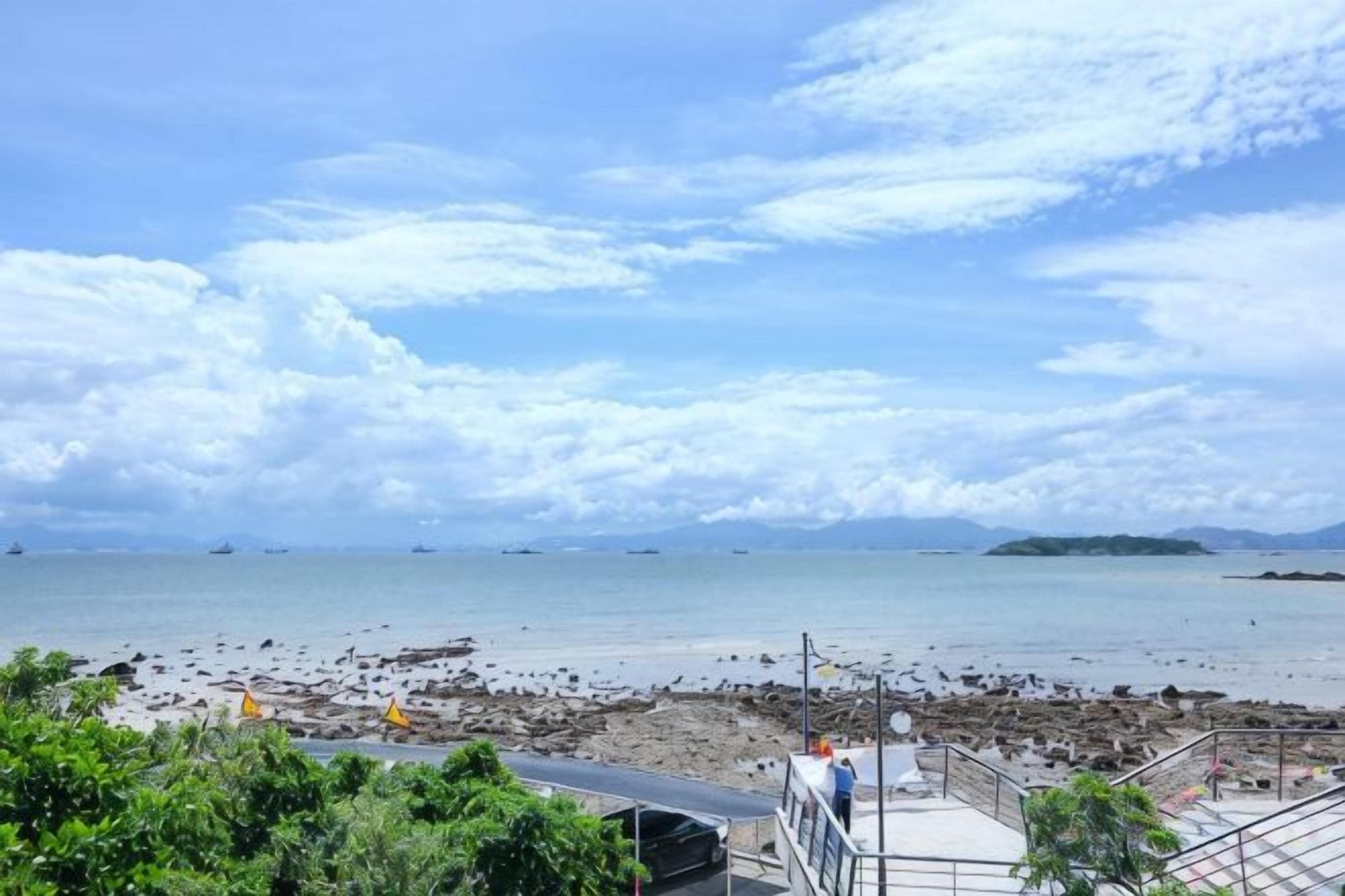 Vista costera con playa, barcos y una isla distante.