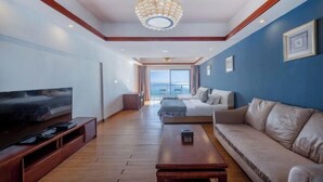 A modern living room with a flat-screen TV, wooden coffee table, beige sofa, and a large window offering a view. - Huidong Biguiyuan Shili Silver Beach Ocean Star Scenic Resort Apartment (Huidong)