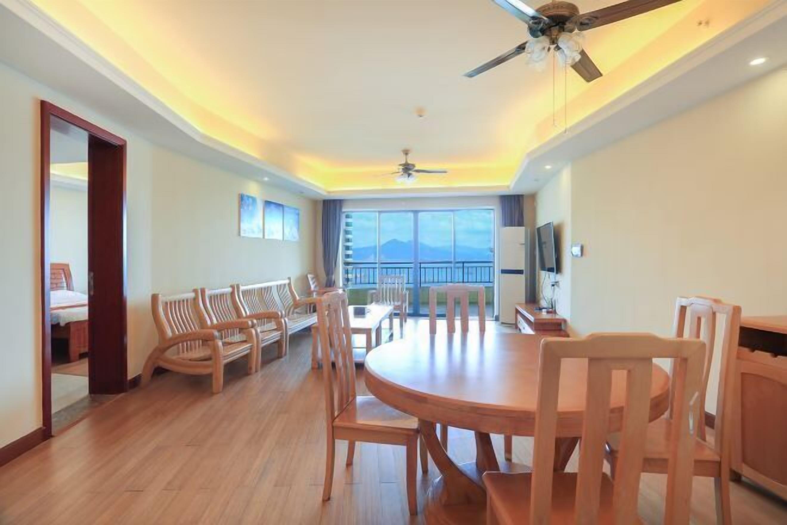 A spacious room with a round wooden table and chairs, a ceiling fan, and a large window offering a view of the mountains.