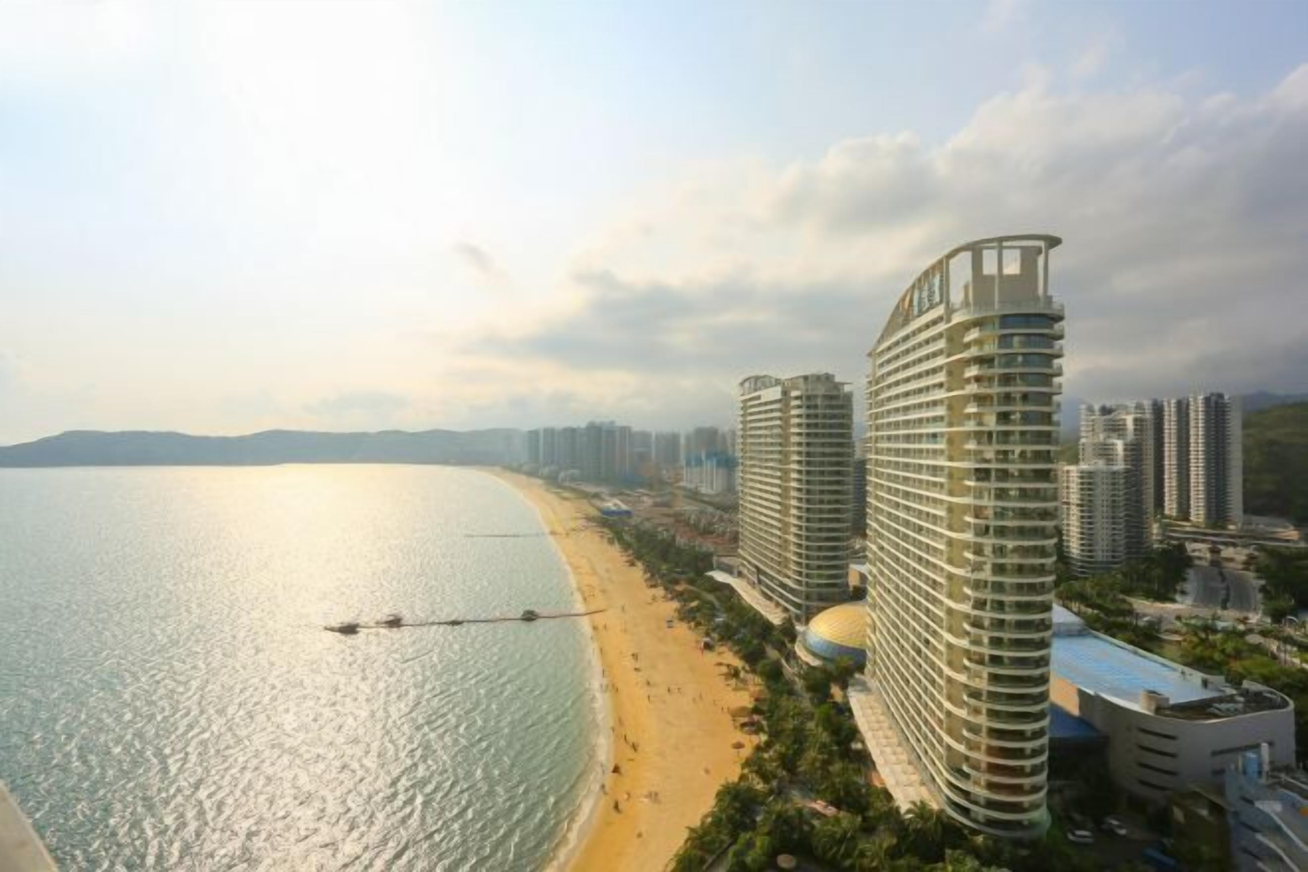 Um hotel costeiro com design curvo, vista para a praia e vários edifícios altos ao fundo.