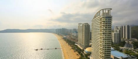 A coastal hotel with a curved design, a beach view, and multiple high-rise buildings in the background.