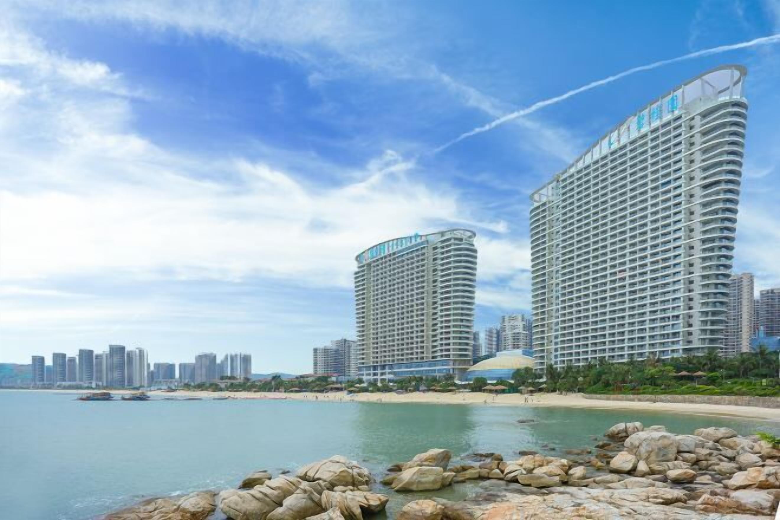 A beachfront hotel with a curved facade, multiple balconies, and a view of the ocean.