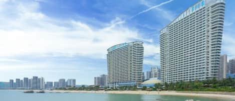 A beachfront hotel with a curved facade, multiple balconies, and a view of the ocean.