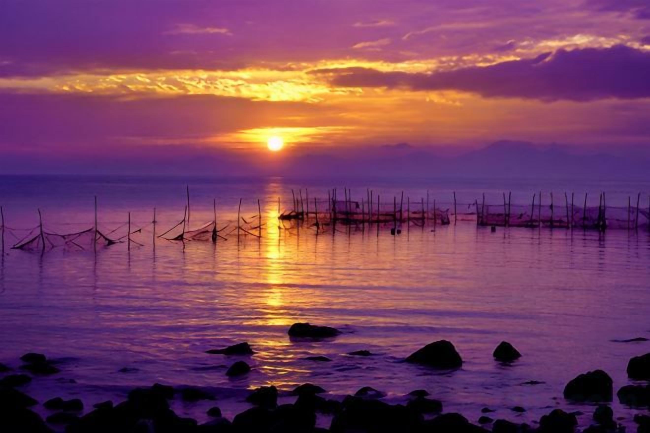 Un coucher de soleil sur une mer calme, avec des filets de pêche au premier plan.
