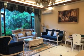 Uma sala de estar com dois sofás, uma mesa de centro, uma mesa de jantar com cadeiras e uma janela grande com cortinas.