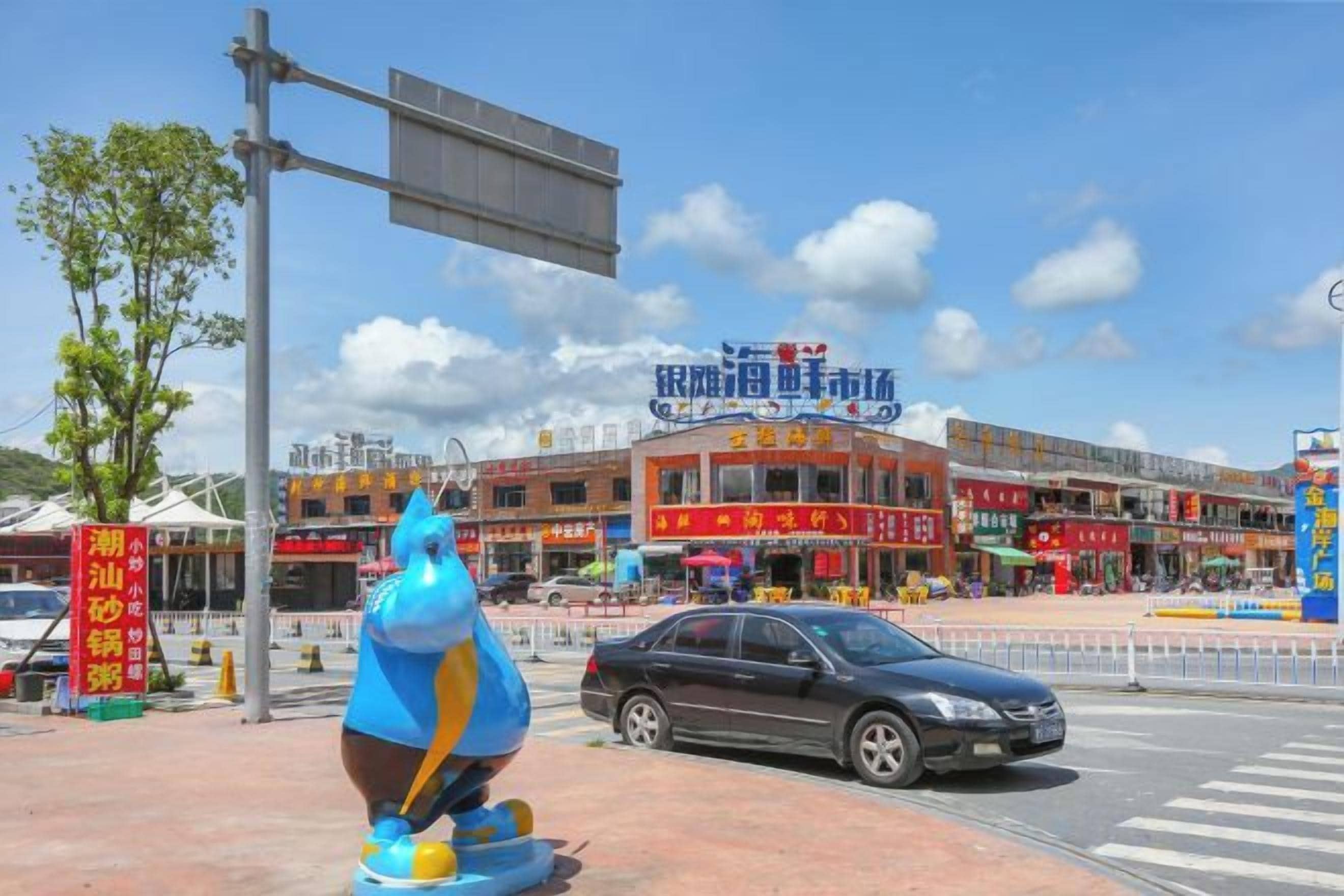 Una escena callejera con una estatua azul, un coche y un edificio con varios letreros.