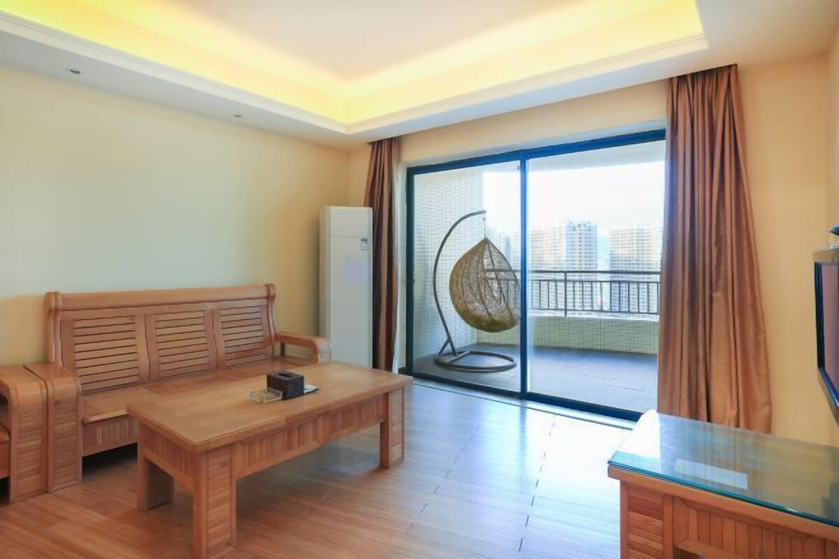 Uma sala de estar moderna com um sofá de madeira, uma mesa de centro de vidro e uma varanda com uma cadeira suspensa.