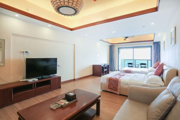 Quarto de hotel moderno com televisão de tela plana, mesa de centro de madeira, sofá e cama com vista para o exterior.