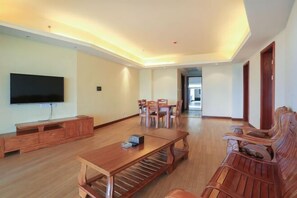Uma sala de estar espaçosa com uma mesa de jantar de madeira, cadeiras, uma TV e um banco de madeira.